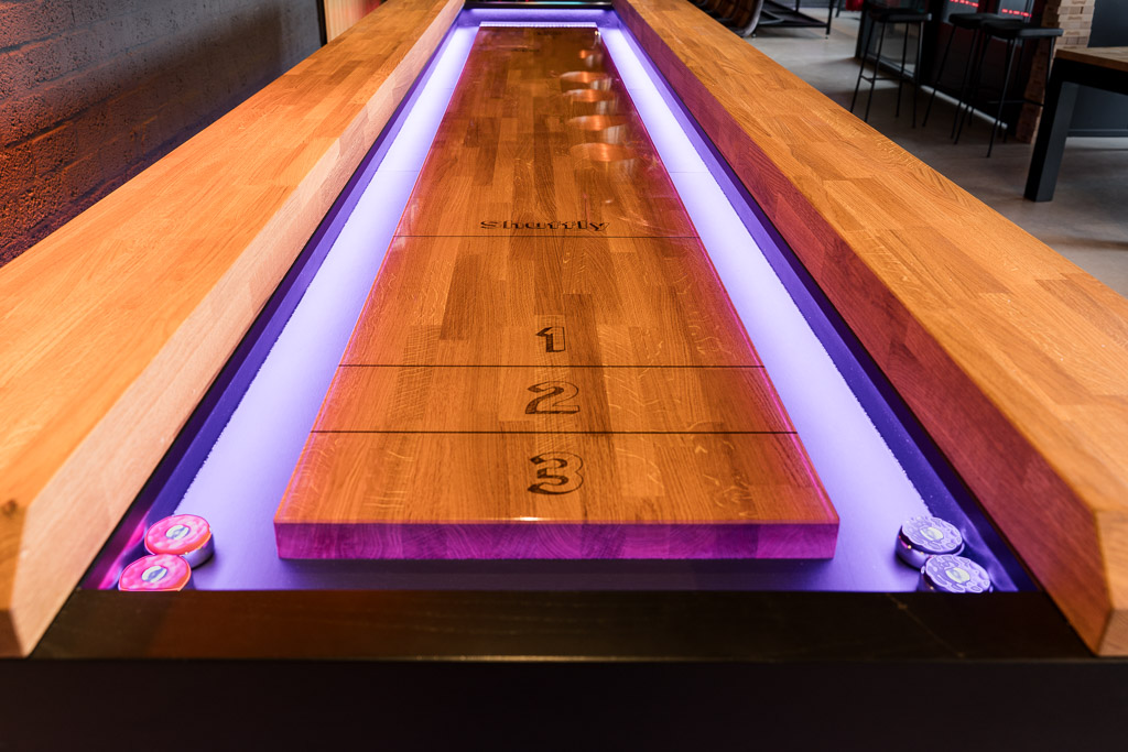Close-up of a shuffleboard playing surface with purple LED lighting along the gutter